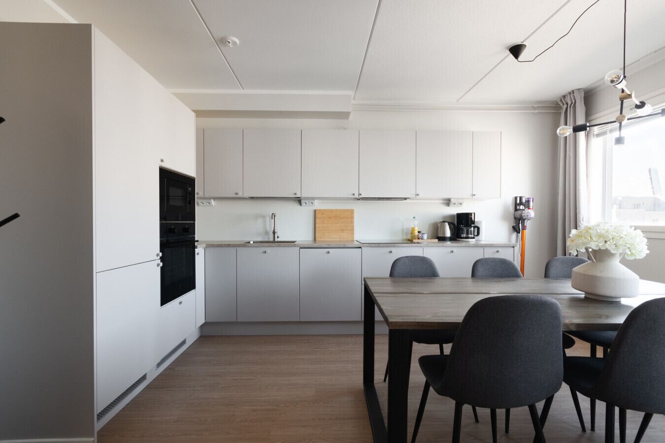 Een moderne keuken met witte kastjes, een houten eettafel en stoelen.