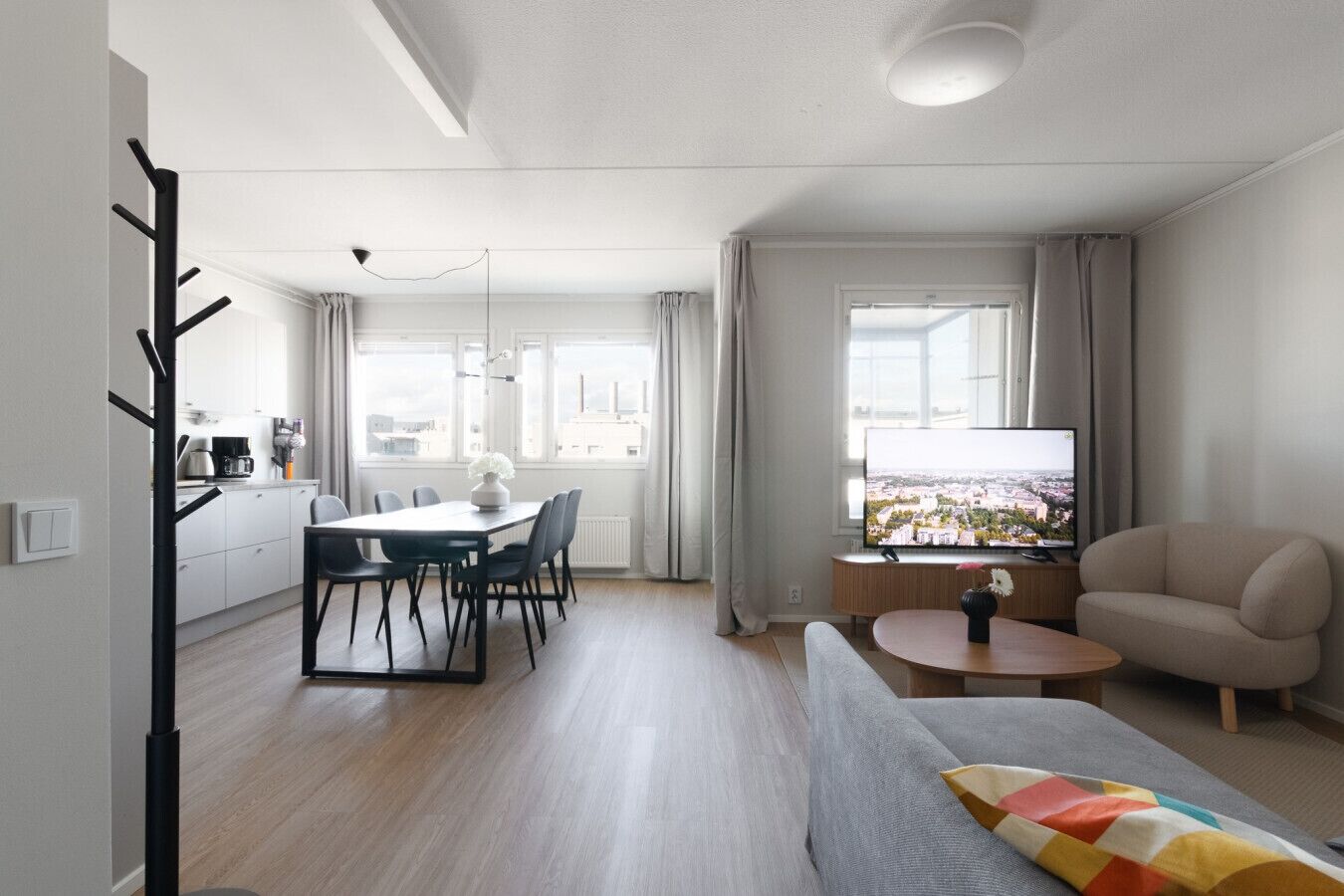 Ein modernes Wohnzimmer mit einer Couch, einem Esstisch mit Stühlen, einem Fernseher und Blick auf eine Stadtlandschaft.