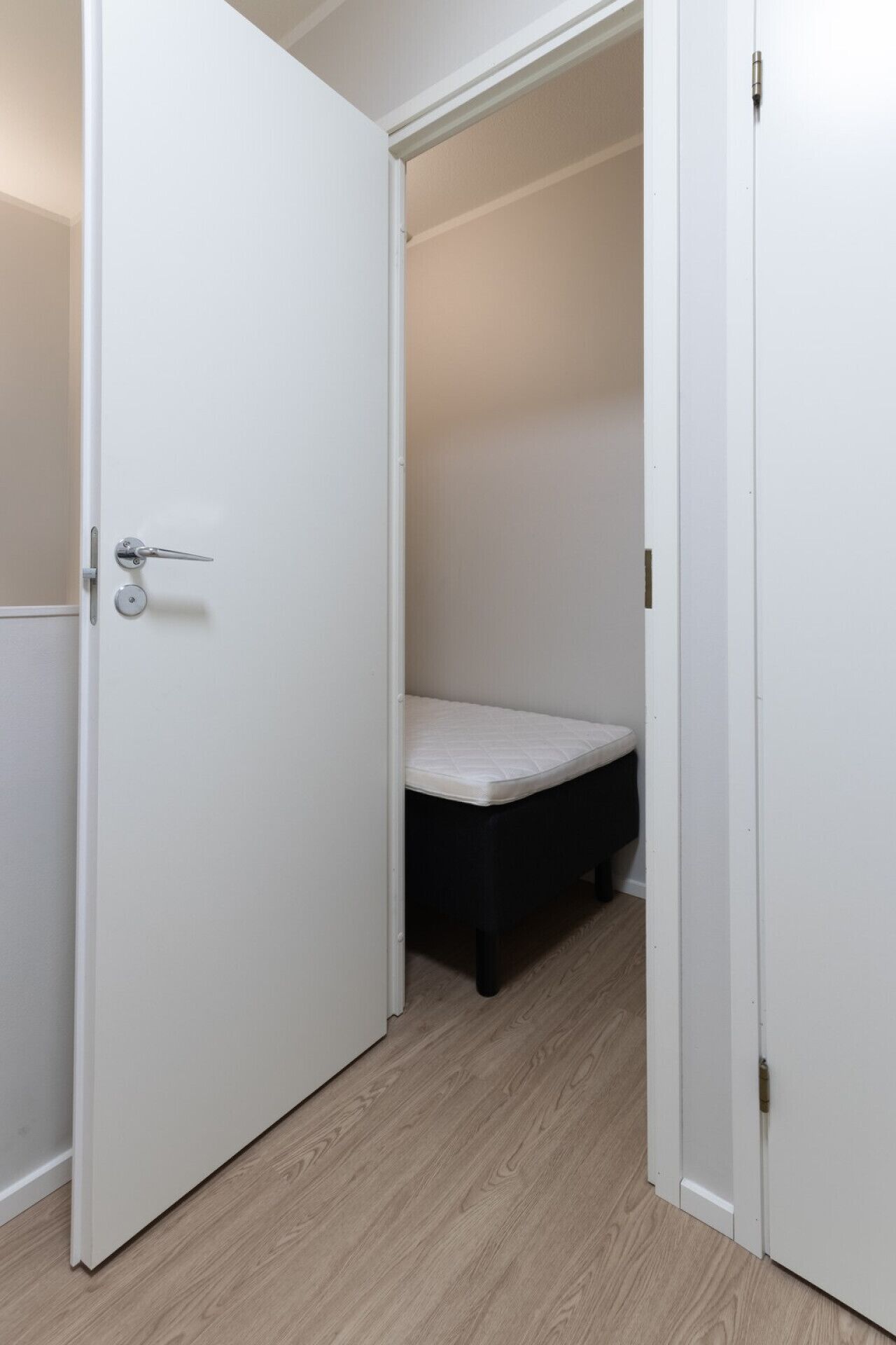 A white door with a silver handle, leading to a room with a mattress on the floor.