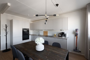 A modern kitchen with white cabinets, a wooden dining table, and a vase of flowers. - Stylish 2-bedroom family apartment w/ sauna, parking (Helsinki)