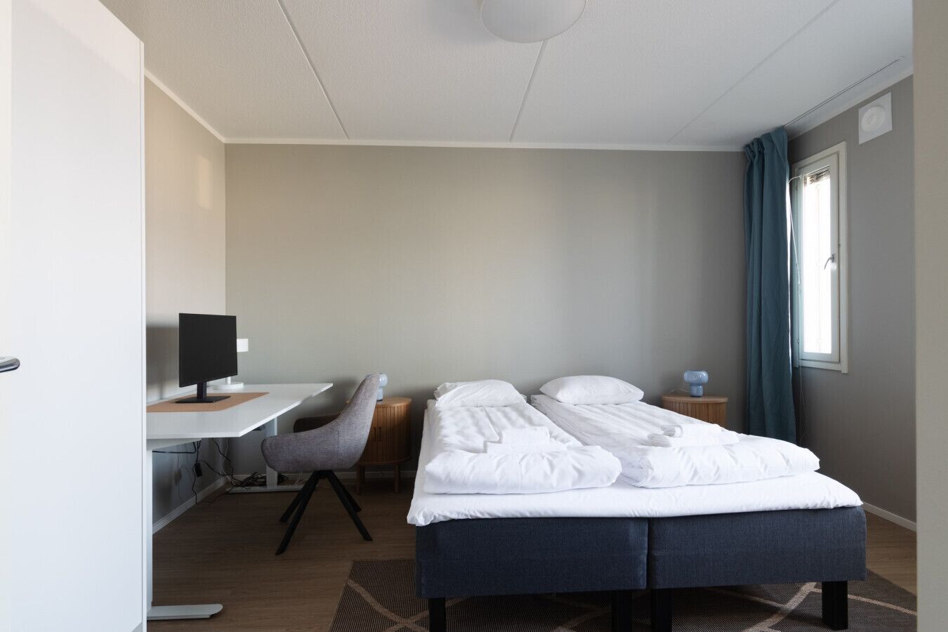 A hotel room with a bed, a desk, a chair, and a computer.