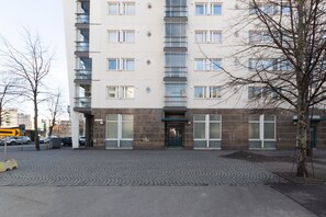 Un immeuble à plusieurs étages avec une entrée au niveau du sol, un espace de stationnement et un arbre au premier plan.