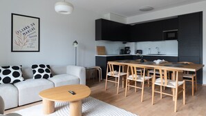 A modern living space with a sofa, coffee table, dining table, and chairs. There is a kitchen area with cabinets and appliances. - Sea view, close to metro, new, 2bedroom apartment (Espoo)