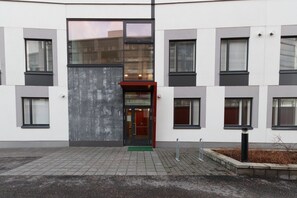 A modern building with a central entrance, multiple windows, and a paved ground area.