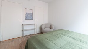 A bedroom with a bed, a chair, a shelf, and a ceiling light. - Sea view, close to metro, new, 2bedroom apartment (Espoo)