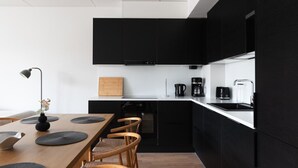 A modern kitchen with black cabinets, a wooden dining table, and a coffee maker. - Sea view, close to metro, new, 2bedroom apartment (Espoo)