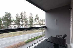 A balcony with a view of a road and trees, a small table, and a chair.