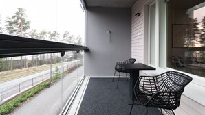 A balcony with a table and chairs, a view of a road and trees, and a glass door. - Sea view, close to metro, new, 2bedroom apartment (Espoo)