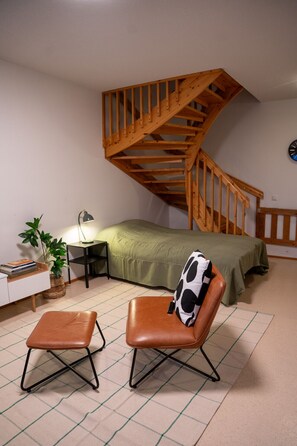 A bedroom with a wooden staircase, a bed with a green cover, a desk with a lamp, and two chairs. - Two-story family apartment for 10 persons with private yard (Rovaniemi)