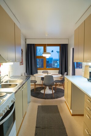 A modern kitchen with a dining area, a stove, and a window with curtains. - Two-story family apartment for 10 persons with private yard (Rovaniemi)