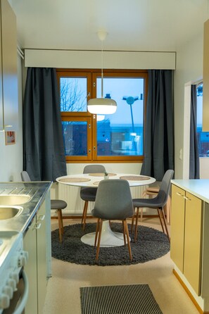 Una cocina moderna con una mesa redonda para comer, sillas, estufa integrada y una ventana con cortinas.
