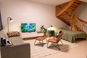 Una sala de estar acogedora con un sofá, un sillón, televisor y una escalera de madera.