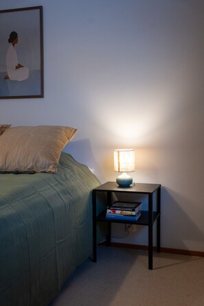 Ein Schlafzimmer mit einem Bett, einem Nachttisch mit einer Lampe und einem Wandbild.