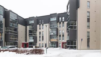 Kerrostalo, jossa on useita kerroksia, parvekkeita, pysäköintialue ja lumipeitteinen maa.