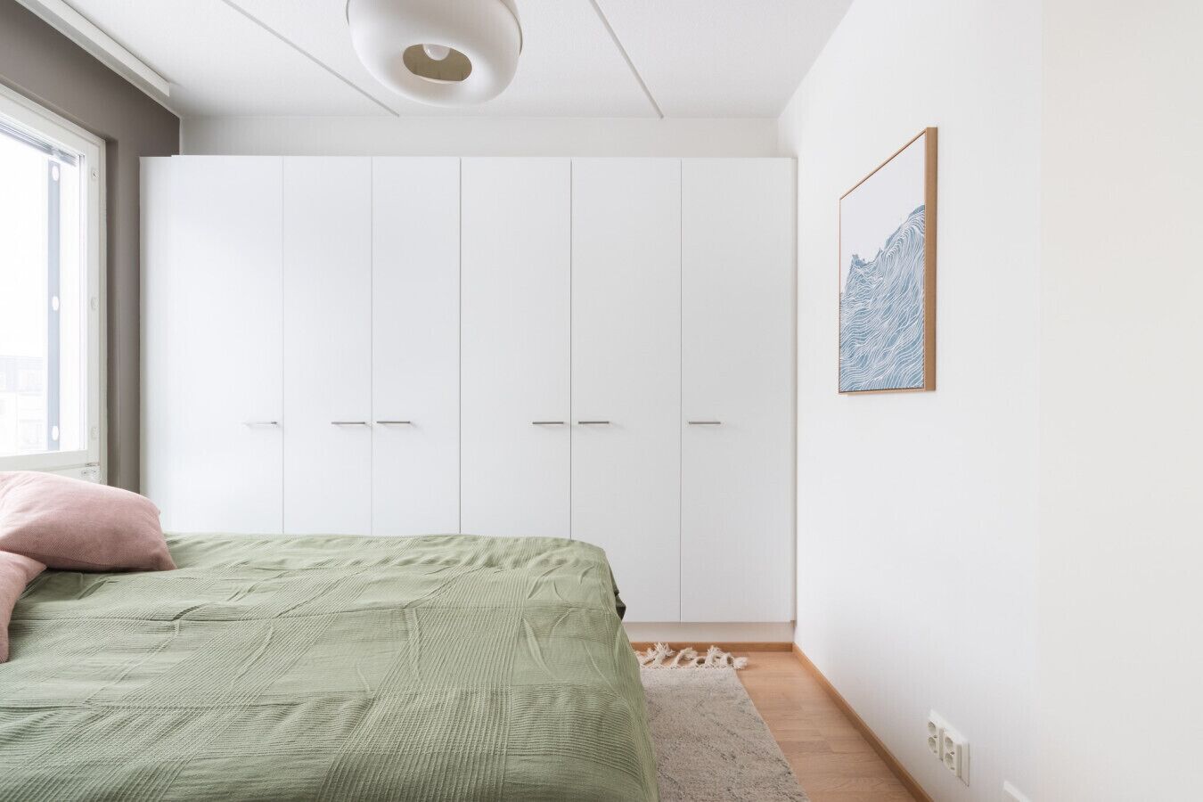 A bedroom with a bed, a wardrobe, a window, and a wall-mounted picture.
