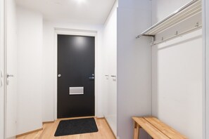 Ein Gang mit einer schwarzen Tür, einer Holzbank und einer weißen Wand mit Lichtschalter.