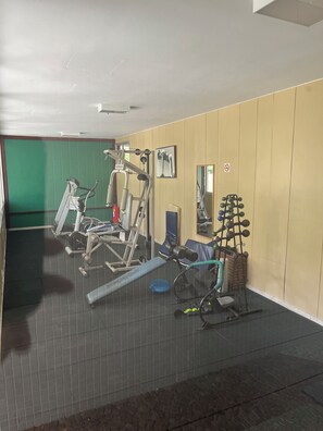 Een fitnessruimte met trainingsapparatuur, een groene wand en een spiegel.