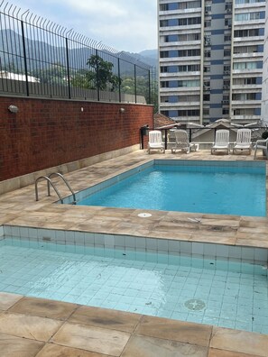 A swimming pool with a tiled edge, a brick wall, and a metal fence. - Dias Ferreira Best Location in Leblon with Pool and Parking Space (Rio de Janeiro)