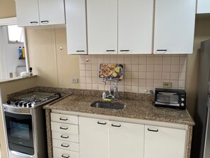 A compact kitchen with a gas stove, a built-in oven, a sink, and a toaster. - Dias Ferreira Best Location in Leblon with Pool and Parking Space (Rio de Janeiro)