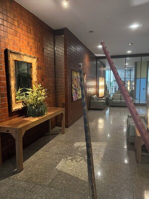 A lobby with a brick wall, a wooden bench, a potted plant, a painting, and a staircase. - Dias Ferreira Best Location in Leblon with Pool and Parking Space (Rio de Janeiro)