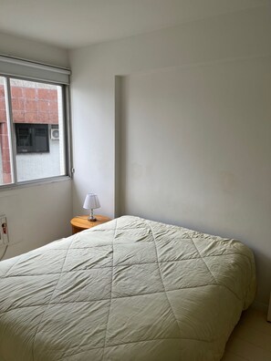A room with a bed, a window, and a small table with a lamp. - Dias Ferreira Best Location in Leblon with Pool and Parking Space (Rio de Janeiro)