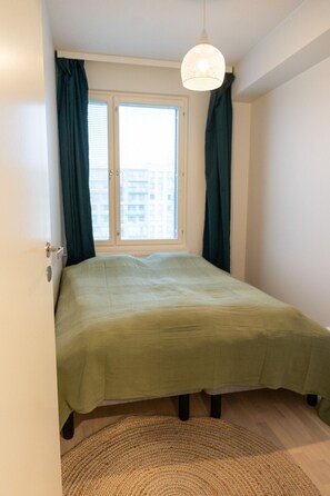 A bedroom with a bed, a window with curtains, a hanging light fixture, and a door.