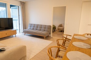 Un salon moderne avec un canapé, un téléviseur posé sur un meuble en bois, une table à manger avec des chaises, et une vue à travers une porte ouverte.