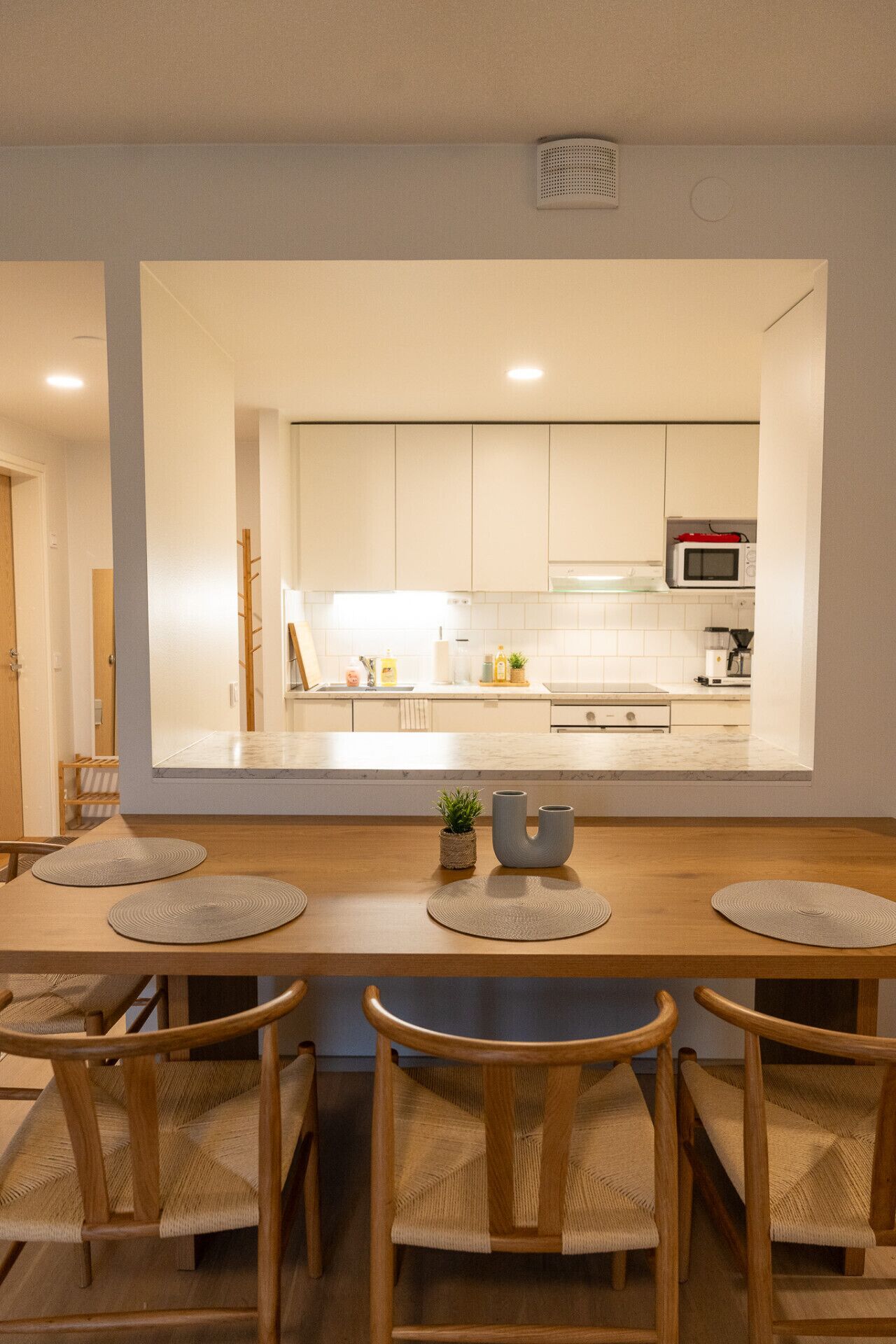 A modern kitchen with white cabinets, a microwave, and a dining area with a wooden table and chairs.