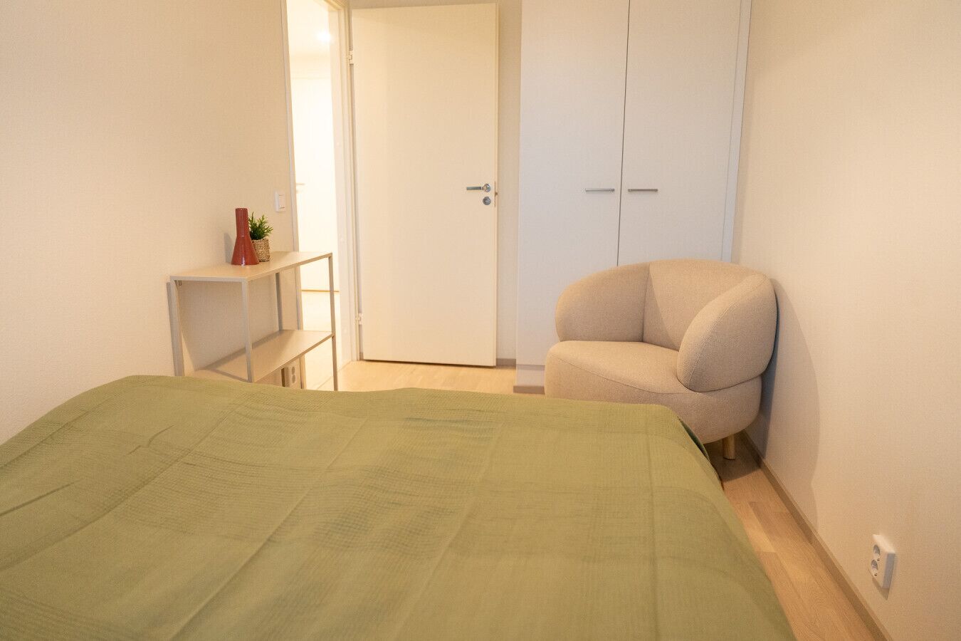 A bedroom with a bed, a chair, a wardrobe, and a desk.