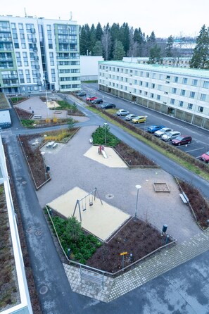 An aerial view of a parking lot with multiple cars, a playground with a slide, and a building complex in the background.