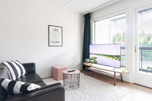 Una sala de estar moderna con un sofá, un televisor sobre un mueble bajo, una mesita redonda y un cuadro en la pared.