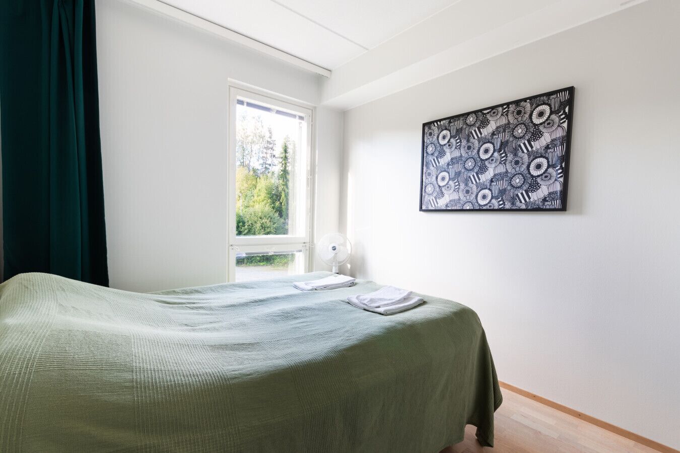 Et soveværelse med en seng, et vindue, et billede på væggen og et natbord med en lampe.