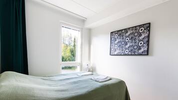 Et soveværelse med en seng, et vindue, et billede på væggen og et natbord med en lampe.