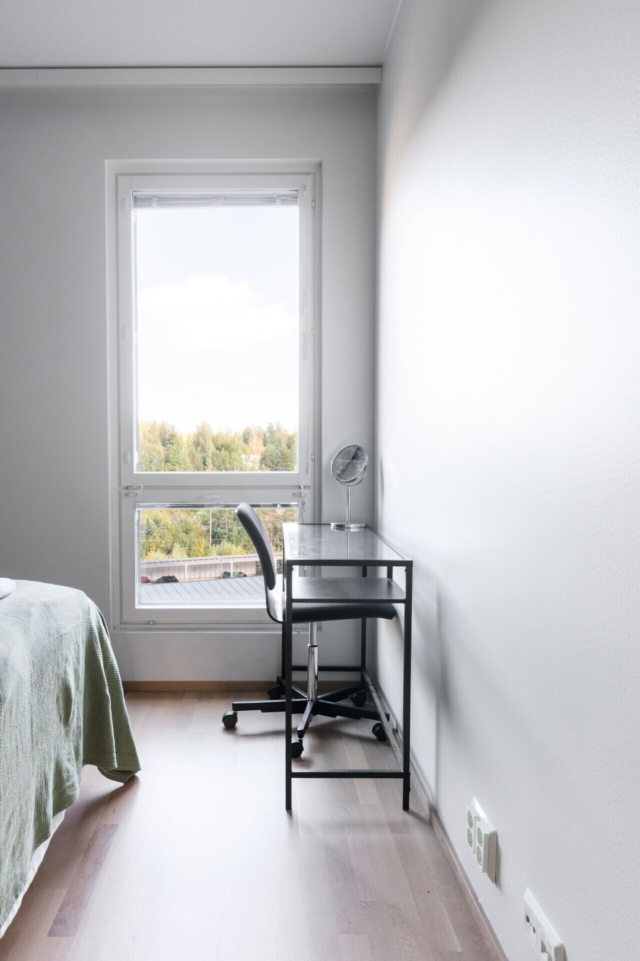 A room with a bed, a desk with a chair, a window, and a view of trees.