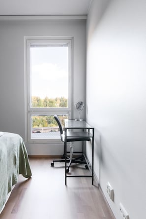 Ein Zimmer mit einem Bett, einem Schreibtisch mit Stuhl, einem Fenster und Blick auf Bäume.