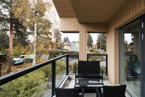 Un balcone con un tavolo e sedie in vetro, affacciato su una zona residenziale con alberi e auto parcheggiate.