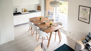 A modern kitchen with white cabinets, a black countertop, and a dining area with a wooden table and white chairs. - Brand new house with four bedrooms, parking, sauna, patio (Vantaa)