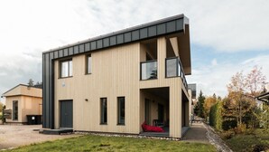A modern two-story building with a flat roof, large windows, and a visible outdoor seating area. - Brand new house with four bedrooms, parking, sauna, patio (Vantaa)