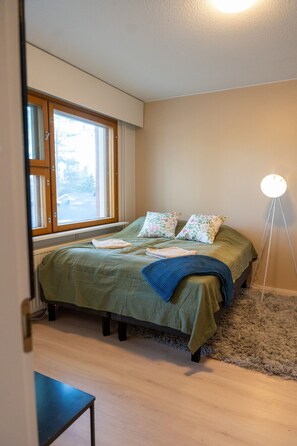 Ein Schlafzimmer mit einem Bett, einem Fenster, einer Nachttischlampe und einem kleinen Tisch.