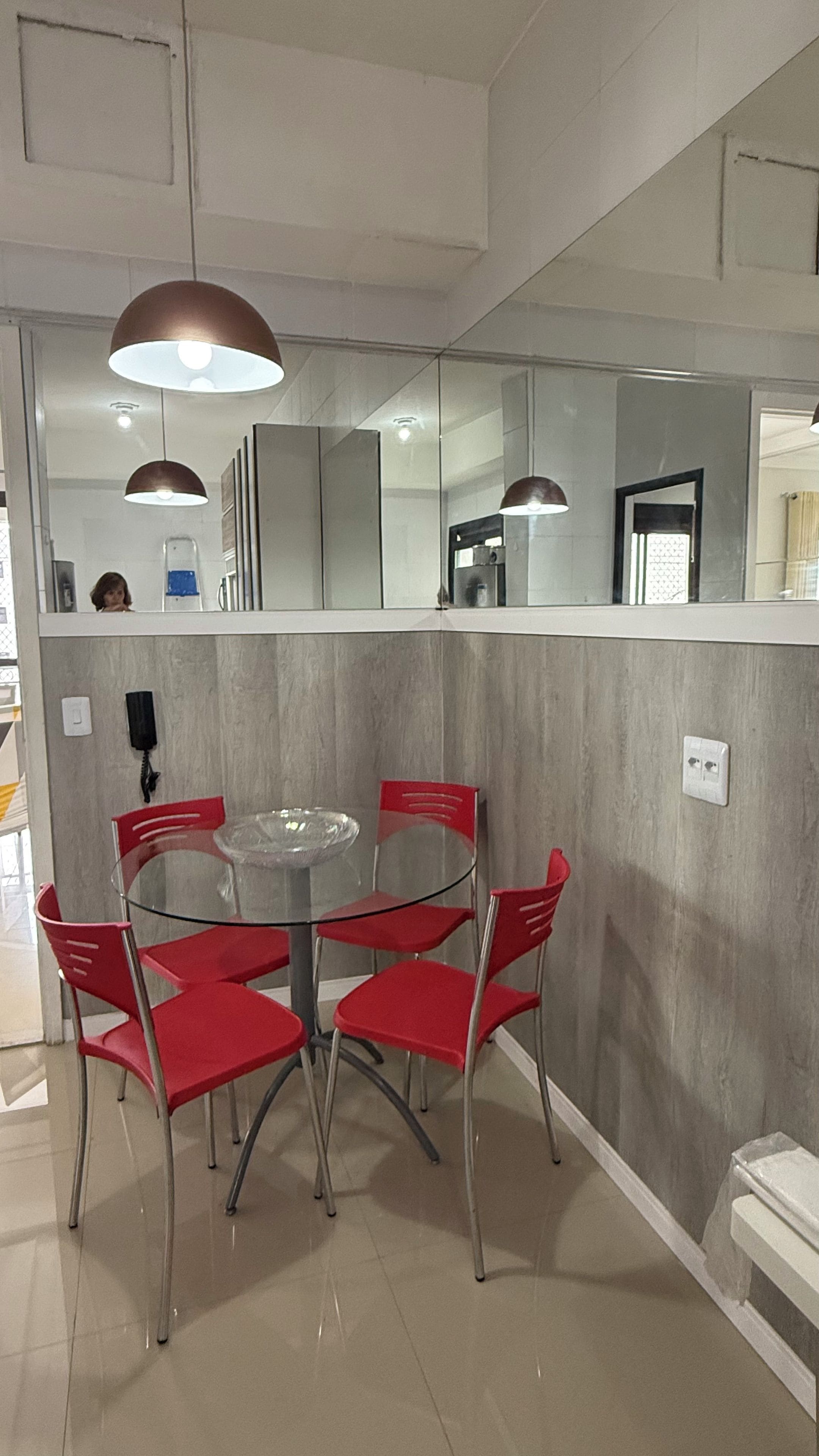 A dining area with a round table and six red chairs, a wall-mounted telephone, and a mirror reflecting the room.
