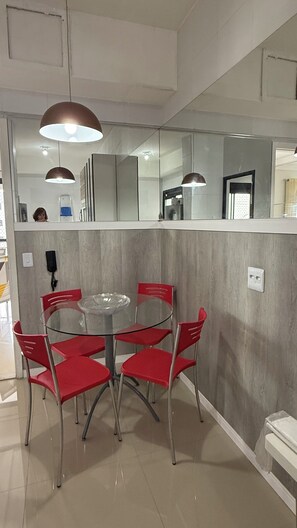 A dining area with a round table and six red chairs, a wall-mounted telephone, and a mirror reflecting the room. - 2802 Parc Apto 3 qtos Luxo com Garagem (Belém)