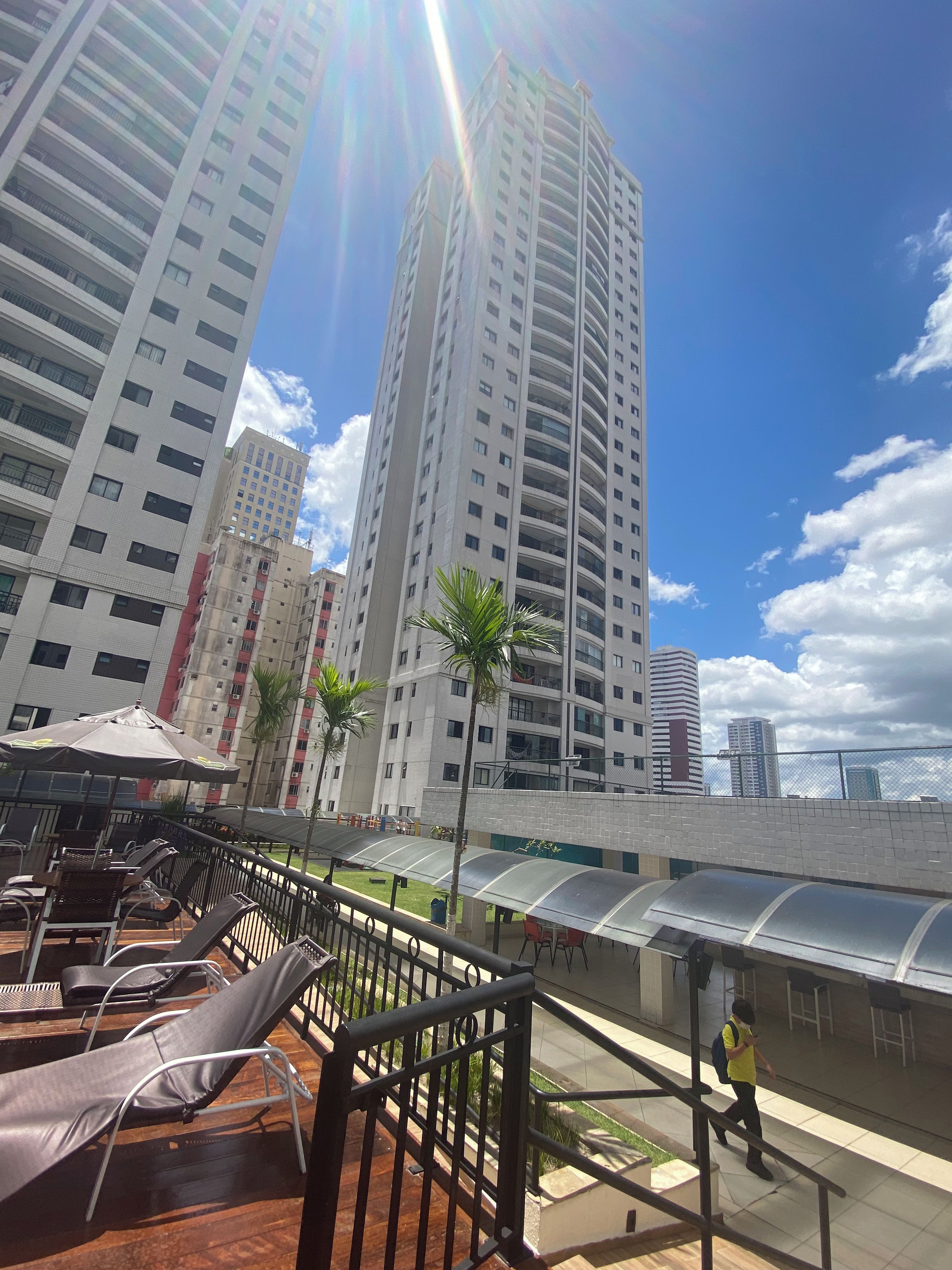 A rooftop terrace with lounge chairs, a covered seating area, and a view of high-rise buildings.