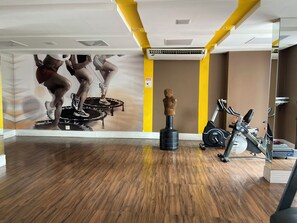 Un gimnasio con equipamiento de ejercicio, piso de madera y una pared con un mural.