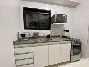 Una cocina compacta con lavamanos, estufa y microondas.