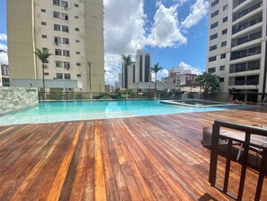A swimming pool with a wooden deck area, surrounded by high-rise buildings. - 2802 Parc Apto 3 qtos Luxo com Garagem (Belém)