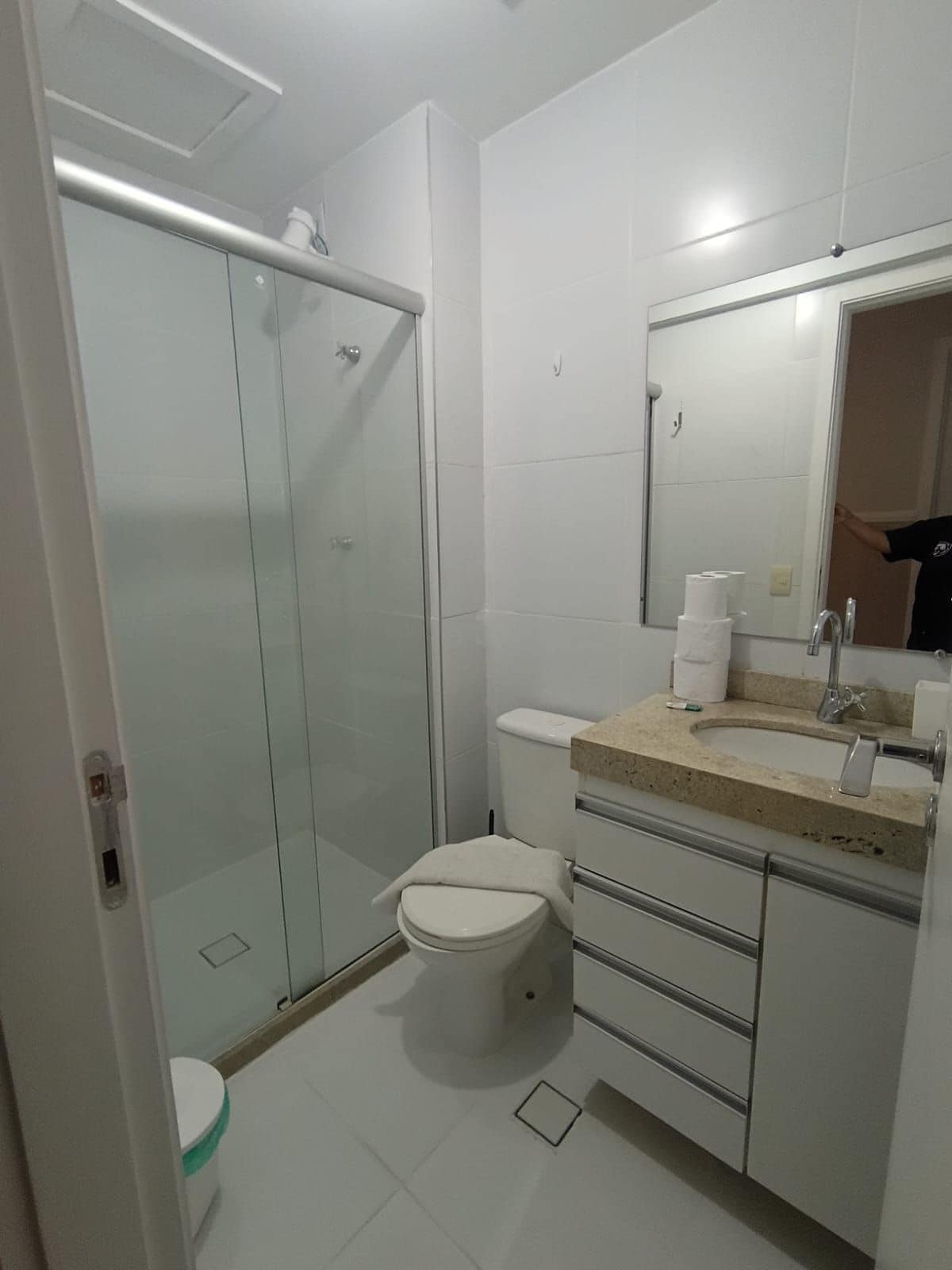 A bathroom with a glass-enclosed shower, a toilet, a sink with a mirror, and a countertop with toiletries.