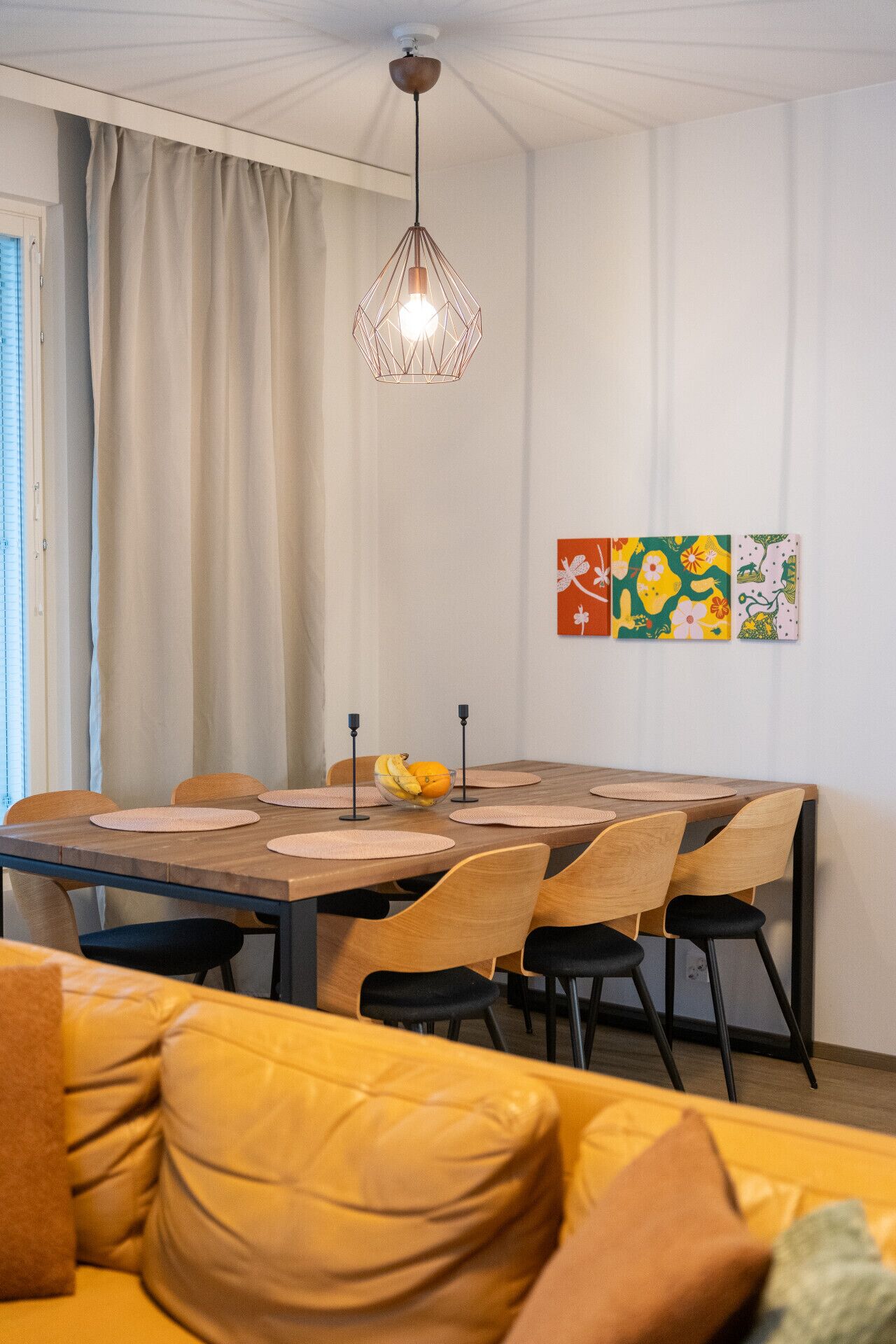 Un coin repas avec une table en bois, des chaises, un saladier de fruits et une suspension.