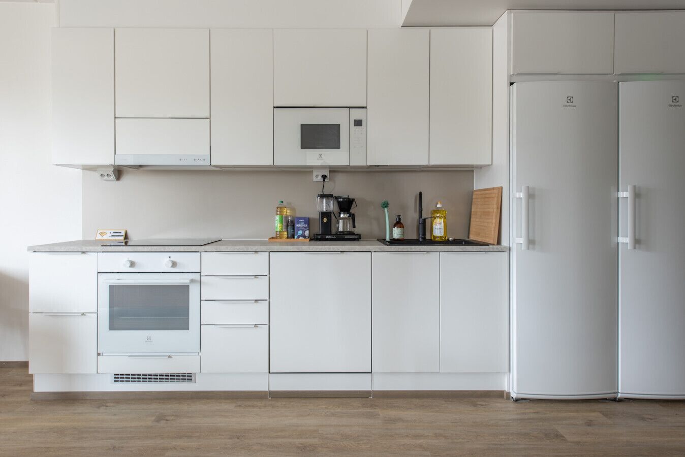 Une cuisine moderne avec des meubles blancs, un four encastré, un four à micro-ondes et un réfrigérateur.