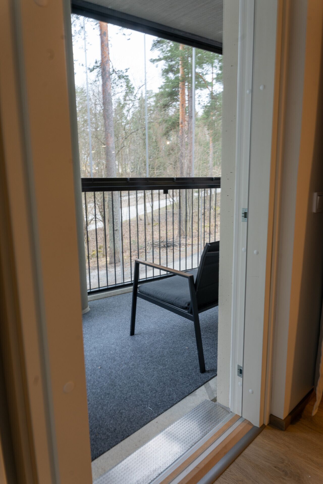 Une pièce avec une porte donnant sur un balcon extérieur, équipé d’une chaise et d’une rambarde.