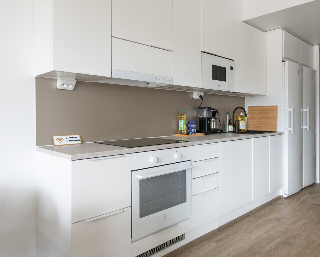 Una cocina moderna con armarios blancos, horno integrado, microondas y cafetera sobre la encimera.